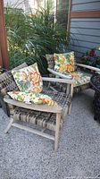 Two wood patio chairs with woven seats and backs, each holding two tropical floral pillows