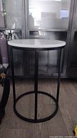 White marble round top plant stand with black metal legs and circular base in a room.