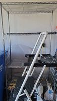 Full view of metal wire rack and step ladder placed inside, showing shelving tiers and step ladder leaning inside rack.