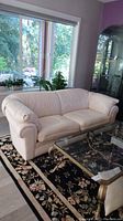 Light beige Benchmark brand sofa placed in living room near large windows, showing front and left side view.