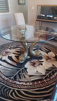 Full view of round glass top table with three brass fish base on floral rug