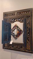 Frontal view of the wall mirror mounted on the wall with one folding door open, showing the mirror inside and other decorative wall art reflected.