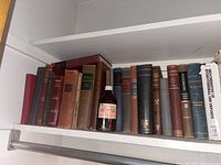 Wide shelf view with antique geology and math books including a science reagent bottle in front