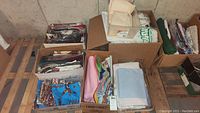 Six boxes of assorted fabric and batting placed on wooden pallettes against basement wall