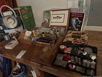 Wide view of wooden table holding fly tying materials, fishing accessories, and books. Includes wooden organizer with fly tying equipment and a plastic tray filled with various hooks, bobbers, and containers.