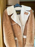 Brown suede shearling coat hanging, showing full front with collar and buttons.