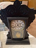Front view of antique key wind mantel clock showing carved dark wood case, clock face with Roman numerals, and floral etched glass panel at bottom