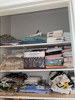 Top three shelves in closet with folded linens, towels, and boxed sheets showing variety of items and some new in packaging.