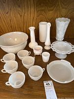 Full view of all 15 milk glass pieces arranged on wooden surface including cups, bowls, vases, and decorative dishes.