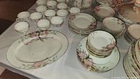 Multiple cups, plates, and platters with floral pattern laid on table