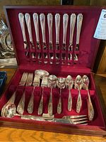 Full view of silver plate flatware set in fitted red velvet-lined case showing knives, forks, spoons and serving utensils arranged inside.