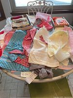 Over 10 vintage aprons spread on table with box of vintage kitchen towels in background