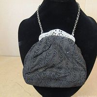 Front view of the antique small clutch purse displayed on a mannequin showing black fabric with a subtle gold wavy pattern and silver frame with chain handle.