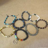 Overview photo of eight bracelets made from a variety of beads including stone, metal, and glass on a beige surface.