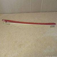 Brass telescoping chandelier candle lighter alongside a red fabric carrying case on a beige surface.