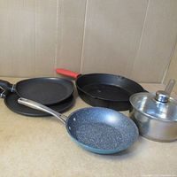 Overview of all five pans including non-stick and cast iron frying pans plus small saucepan with lid