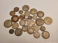 Top-down view of 27 assorted European silver coins laid out on white background, showing varied designs and sizes.