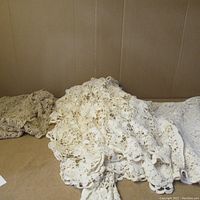 Close-up of a cream/white hand-knit crocheted lace textile showing intricate floral lace patterns and delicate stitching, used vintage condition.