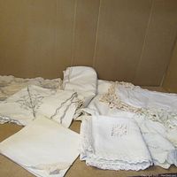 Lot of assorted white hand-knit doilies and textiles laid out, showing various folded and flat pieces with lace and embroidery details.
