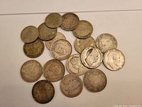 Overhead view of 16 scattered silver coins on white surface