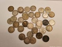 Top-down group shot of all 35 silver sixpence coins arranged on a white surface showing some of both obverse and reverse sides.