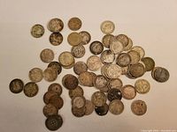Top view showing entire lot of silver British and Commonwealth three pence coins arranged loosely on a white surface, varying degrees of wear and tarnish.