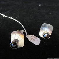Pair of silver cufflinks with dark pearls placed on black background. Price tag visible.