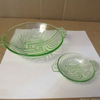 Two green glass bowls with Art Deco patterns and decorative handles on a white background.