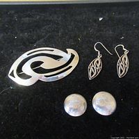 Photo showing the sterling silver pin and two sets of earrings arranged on black fabric.