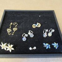 Top-down view of all seven pairs of vintage earrings arranged on black velvet showing variety of styles and stones