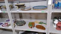Shelf displaying several wood and resin art pieces including lazy Susan, footed dishes, cutting boards with resin handles, and decorative wooden items with resin accents.