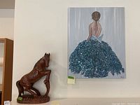 View of the wood horse carving beside the mixed media painting on canvas hanging on the wall.
