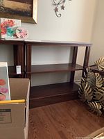 Front view of dark brown wooden bookcase with three shelves alongside other items partially visible.