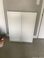 Front view of the white double door cabinet against a wall on carpet floor.