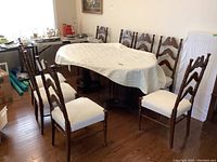View of eight wooden dining chairs positioned around a table with a white tablecloth, showing the style and number of chairs.