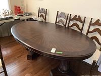 Oval wood dining table with polished dark veneer, pedestal base, no visible marks