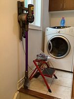 Vacuum mounted on wall bracket with wand, cleaner head and two tools attached