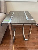 Side view of an end table showing composite wood top with chrome metal L-shaped inlay and chrome metal legs