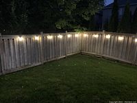 Two strings of outdoor lights shown illuminated on wooden fence during night, displaying warm white globe bulbs and black wiring.