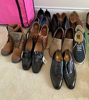 Overview of all 11 pairs of men's shoes arranged on carpet including boots, dress shoes, loafers, casual shoes.