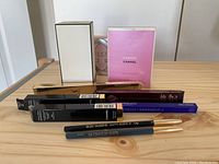 Seven cosmetic pencils in packaging and three boxed perfume/cosmetic products arranged on a wooden surface, close-up view