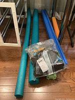 Photo showing the pool noodles and sealed bag of gloves under a table, highlighting colors and bag contents