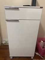 Front view of the white rolling cabinet showing the drawer and cupboard door with metal handles.