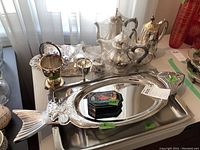 Overview of tea service, tall coffee pot, silver trays including large fish-shaped tray, painted box on top of rectangular tray