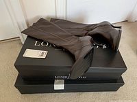 Three pairs of brown knee-high leather boots stacked on two London Fog branded shoeboxes.