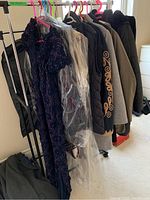Photo showing a rack of womenswear including the beaded formal dress, other dresses covered in plastic, and several jackets and outerwear in neutral and dark colors.