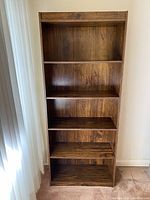 Front view of tall wooden book shelf with five shelves and a rich brown grain finish.