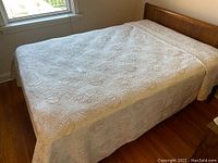 Bedspread laid out over a double bed, showing the embossed floral pattern and full coverage on sides.