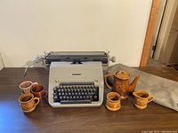 Full overview of Facit typewriter with five brown embossed ceramic mugs and one matching brown ceramic teapot on table