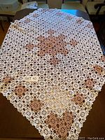 Crocheted table cloth laid out flat on a wooden table showing full pattern and colors.